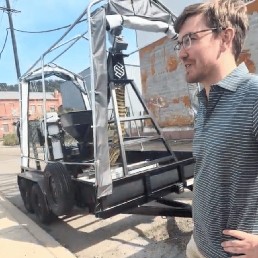 A team member standing beside the trailer-mounted Silly Surfacing pothole repair robot